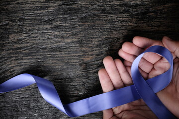 Top view of male hand holding periwinkle blue ribbon on wood background with copy space. Stomach...