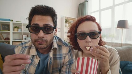 Close-up POV of red-haired Caucasian woman sitting next to young Mixed-race man at home. Couple wearing 3D glasses, eating popcorn, watching interesting movie in living room - Powered by Adobe