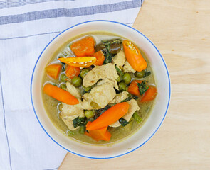 Thai green curry with chicken, carrots, eggplants and sweet basils in a bowl on a light brown background with a napkin on it (Famous Thai food)