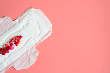 Obraz premium women's menstrual sanitary pad or napkin for normal profusion of secretions with red and pink beads in the shape of hearts as an imitation of blood on pink background