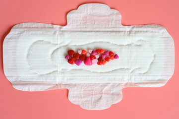 women's menstrual sanitary pad or napkin for normal profusion of secretions with red and pink beads in the shape of hearts as an imitation of blood on pink background