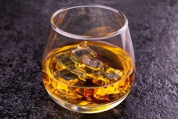 Glass of cognac with ice on a black background.