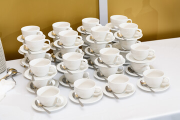 group of empty white cups and saucers with a teaspoon. Many rows of white cups of tea, standing on top of each other, for serving for breakfast or buffet at the seminar.