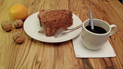 on a wooden table a plate with cake, a cup of coffee or chocolate, tangerine and nuts