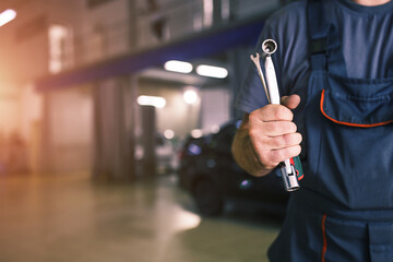 The hand of a car repairman with keys and a special tool on the background of the service area. A mechanic in a car service station in uniform. Copy space