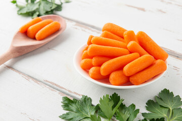 Small peeled pieces of carrot in plate on white wooden table.