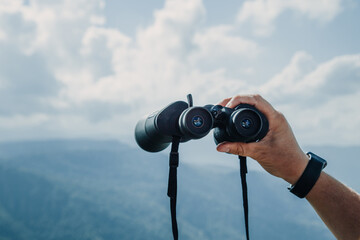 Hands holding binoculars on mountains forest nature background, looking through binoculars, travel,...