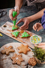 Girl and mom decorate gingerbread cookies. Homemade traditional Christmas pastries. Delicious dessert. Hands of people close up. Vertical shot