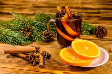 Cup of mulled wine with cinnamon, sliced orange and fir tree branches on wooden table