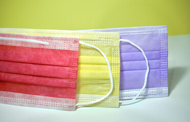 Colorful (red, yellow, purple, pink) medical masks on white ground and yellow background.