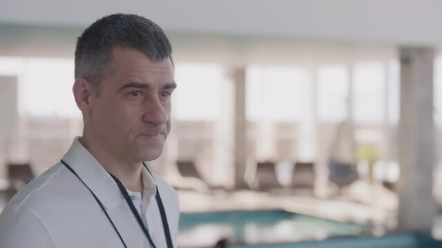 Medium shot of middle-aged male swimming coach blowing whistle in indoor pool