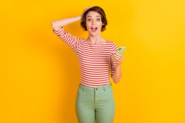 Portrait of nice person shocked hand on head open mouth hold smartphone isolated on yellow color background