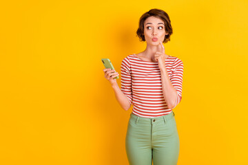Photo of attractive intelligent person watch empty space finger on chin hold phone isolated on yellow color background