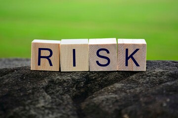 Risk text on wooden cube block on top of big stone with blurred background