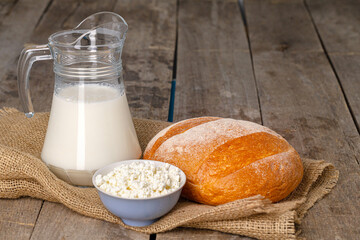 Glass jar of milk, bowl of cottage cheese and bread on wooden table