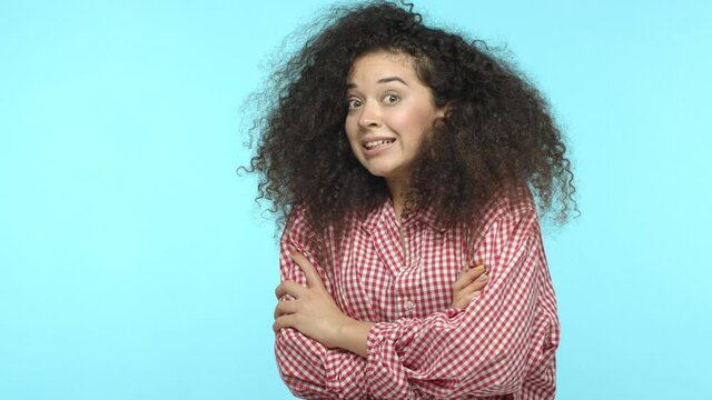 Slow motion of startled woman jumping surprised and gasping, smiling awkward at camera, standing against turquoise background