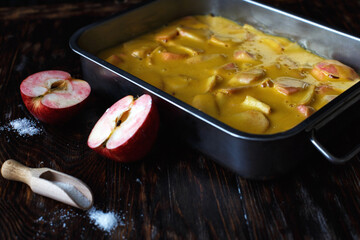 Making an apple pie. Raw dough in a baking dish, apple and sugar on the wooden table