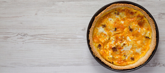 Homemade Bacon Quiche with Eggs and Cheddar Cheese on a white wooden surface, overhead view. Flat lay, from above, top view. Space for text.