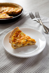 Homemade Bacon Quiche with Eggs and Cheddar Cheese on a white plate, side view.