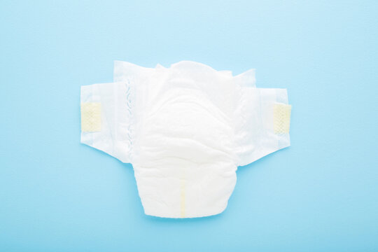 White, soft, new baby diaper on light blue table background. Pastel color. Closeup. Top down view.