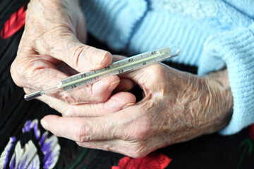 A 90-year-old grandmother holds a mercury thermometer in her hands. Protecting older people in quarantine.