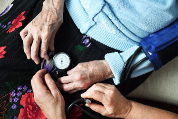 A doctor measures the blood pressure of a 90 year old female patient. Medicine and health concept.