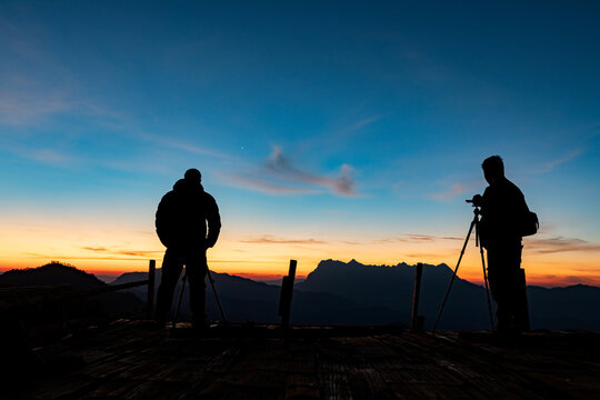Silhouette photographer take photos early morning mountains view with smooth orange blue gradient of dawn sky.