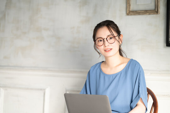 パソコンを使いながらリモートワークのミーティングをする何かに気が付いた眼鏡の若い日本人女性1　コピースペースあり