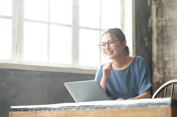 パソコンを使いながらZoomなどでリモートワークのミーティングをする笑顔が美しい眼鏡の若い日本人女性1　コピースペースあり