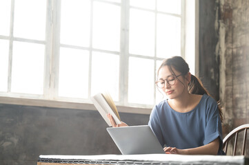 パソコンと本を開いて調べながら仕事をする美しい眼鏡の似合う日本人女性5 バストアップ　コピースペースあり　煽り広角
