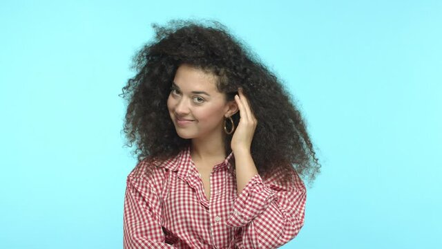 Romance and valentines day concept. Coquettish young woman with curly hair, flirting with you, tuck strand behind ear and glancing at camera, smling seductive, standing over turquoise background