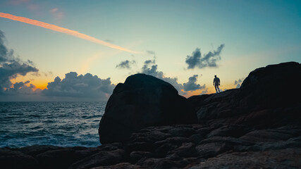 Silhouette of a man standing on the rocks by the sea at sunrise