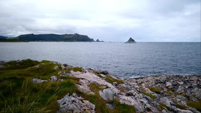 Rocks on the coast of And&oslash;ya island in the Norwegian Sea near village Bleik, Vester&aring;len, Norway with small surf, coastline and bird rock Bleiks&oslash;ya on the horizon on cloudy day in late summer.