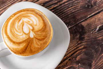Delicious Cup of hot cappucino is on the wooden table. It is an art on the latte.