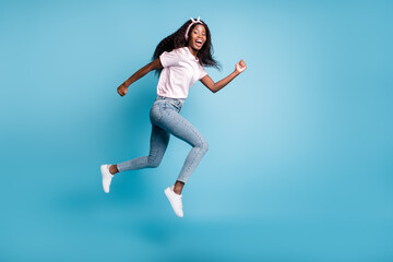 Full length photo of cute shiny afro woman wear pink t-shirt jumping running hands arms fists isolated blue color background