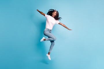 Full length photo of charming cute afro woman wear pink t-shirt jumping hands arms sides isolated blue color background