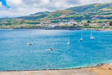 Boats on the water of Praia da Vitória bay with typical Azorean mountains as background in...