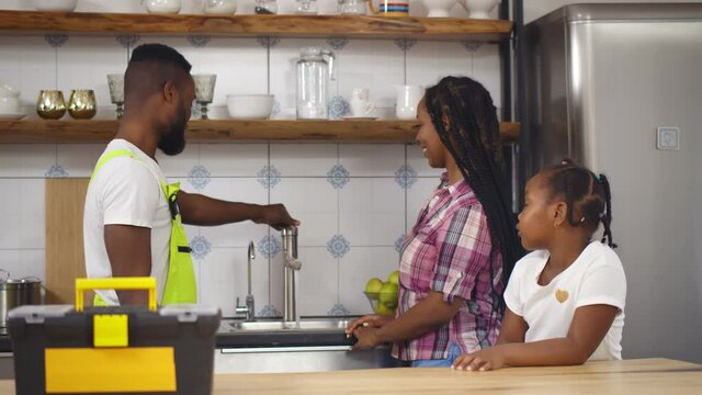 African plumber repairing running water for mother and daughter