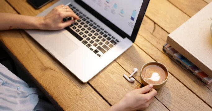 Female working on laptop and drinking coffee with a heart shape. High angle, close-up tracking shot.