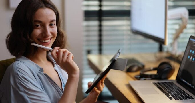 Portrait of a cheerful young woman working on a digital tablet at home office. Handheld medium shot. Concept of creative work on digital devices and work at home