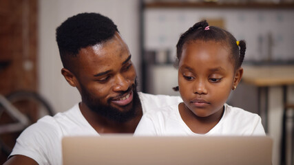 African american father and daughter using laptop at home together