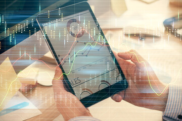 Double exposure of man's hands holding and using a phone and financial graph drawing. Analysis concept.
