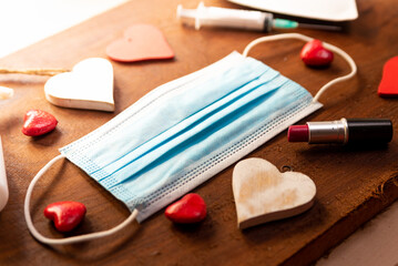 Obraz na płótnie Canvas covid valentine's day hygiene concept. face mask with red hearts on wooden background. top view of hand sanitizer and lipstick and syringe for holiday in the new normal
