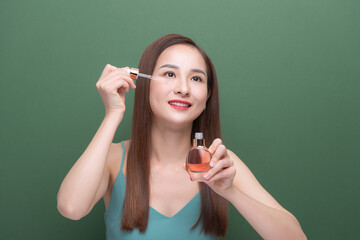 Obraz premium Young amazing Asian woman posing isolated over green background wall holding oil drop serum.