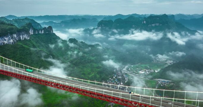 Timelapse Aerial view of Aizhai Bridge in a cloudy day, suspension bridge across valley with symbolic red color in Aizhai, western Huhan, China. One of highest and longest suspension bridges in world.