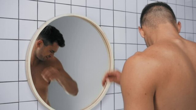 displeased man smelling armpits and grimacing in bathroom