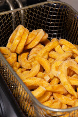 Frozen curly fries, coated in herbs and spices, cooking in a deep fat fryer basket.  Fast food concept
