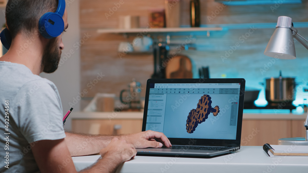 Poster man architect with wireless headset using laptop while working at home at night sitting in the kitch