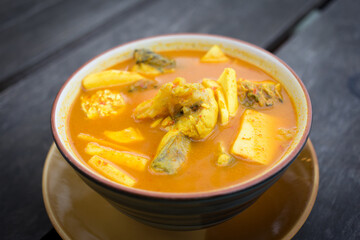 Spicy sour yellow curry with  coconut shoots and sea fish is one of Southern of Thai food on wood table as a background.