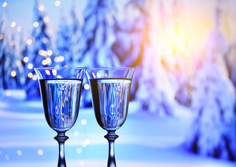 Glasses with sparkling champagne against the background of a winter landscape of snow-covered fir trees.